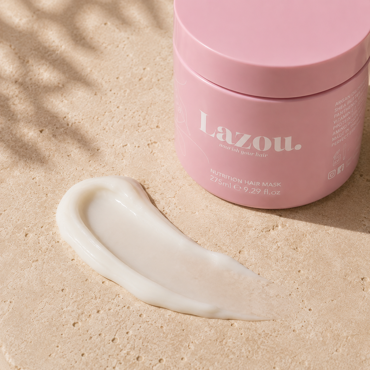 Pink jar of Lazou hair mask with a dollop of cream on a beige surface